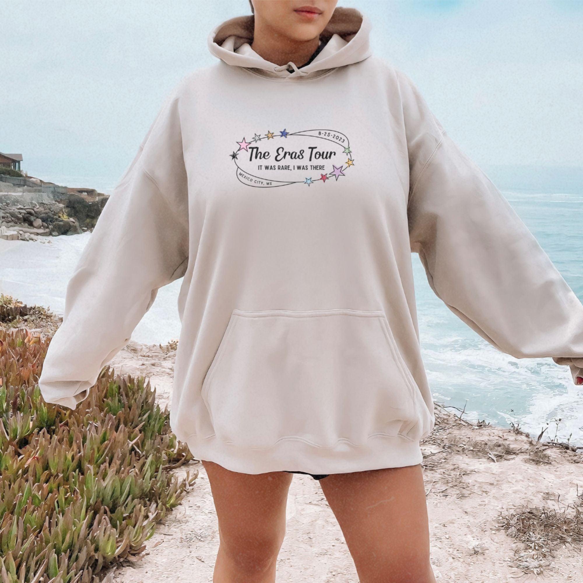 a woman standing on a beach wearing a hoodie
