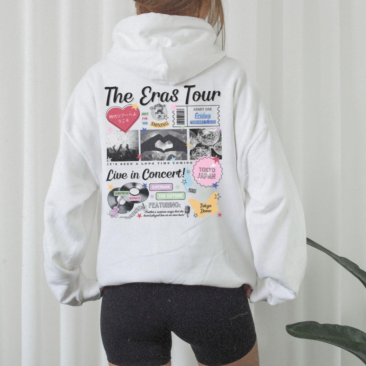 a woman wearing a white hoodie with the words the eras tour printed on it