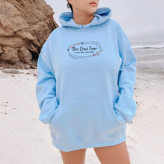 a woman standing on a beach wearing a blue hoodie