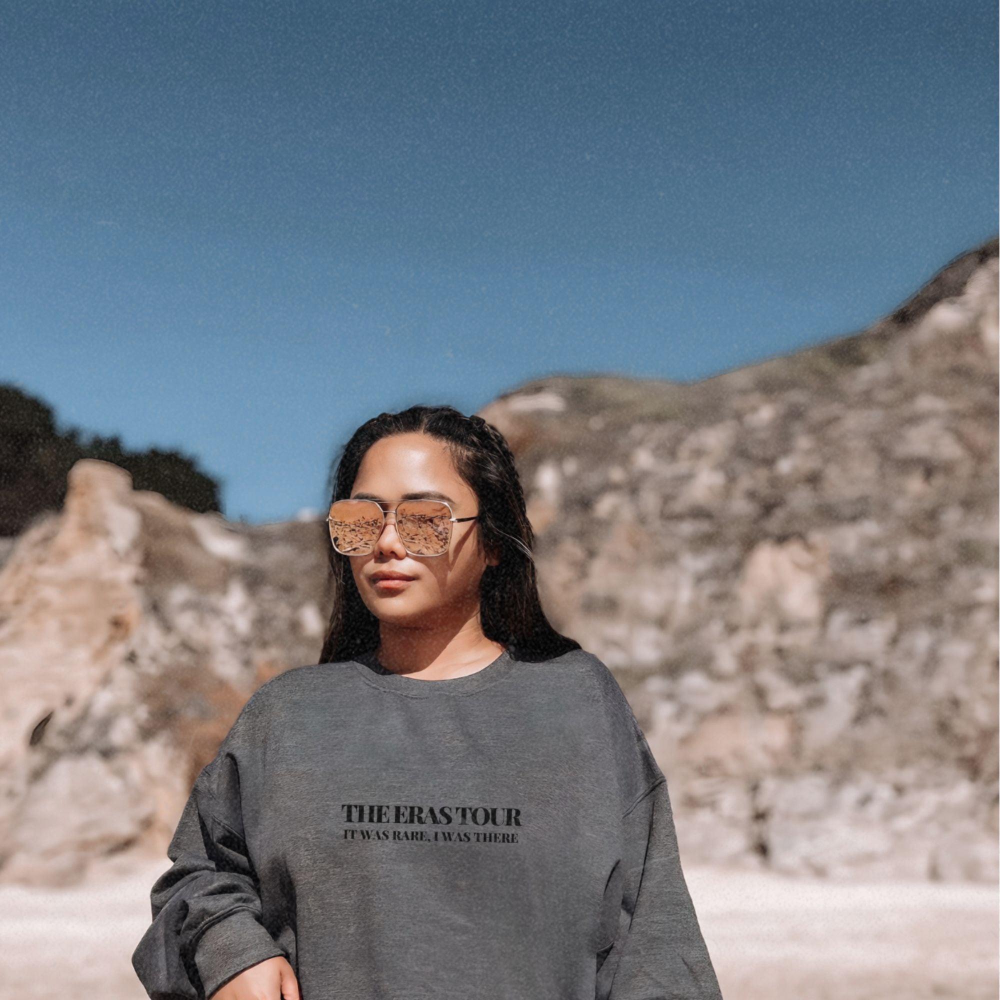 a woman wearing a sweatshirt and glasses standing in front of a mountain