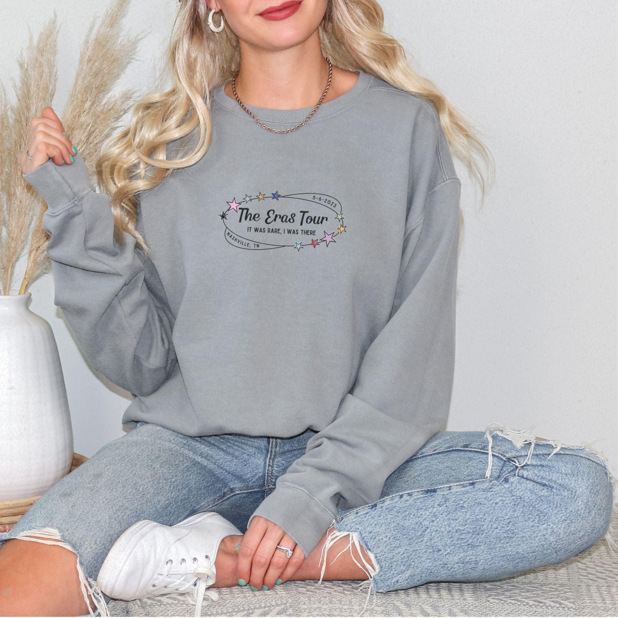 a woman sitting on a bed wearing a grey sweatshirt