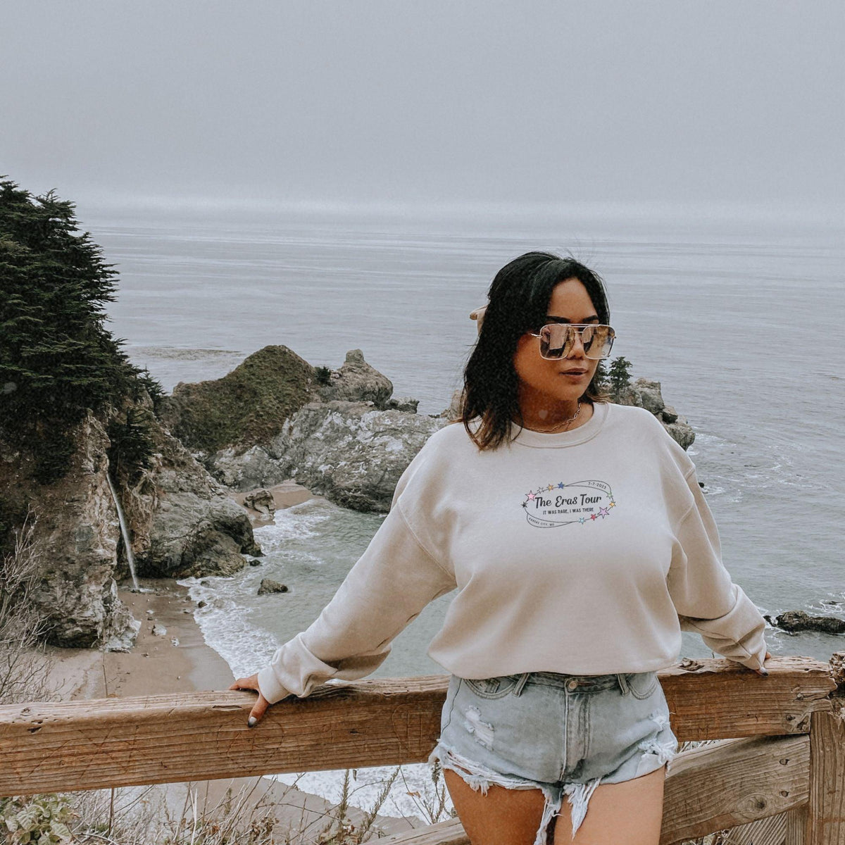 a woman standing on top of a wooden fence next to the ocean
