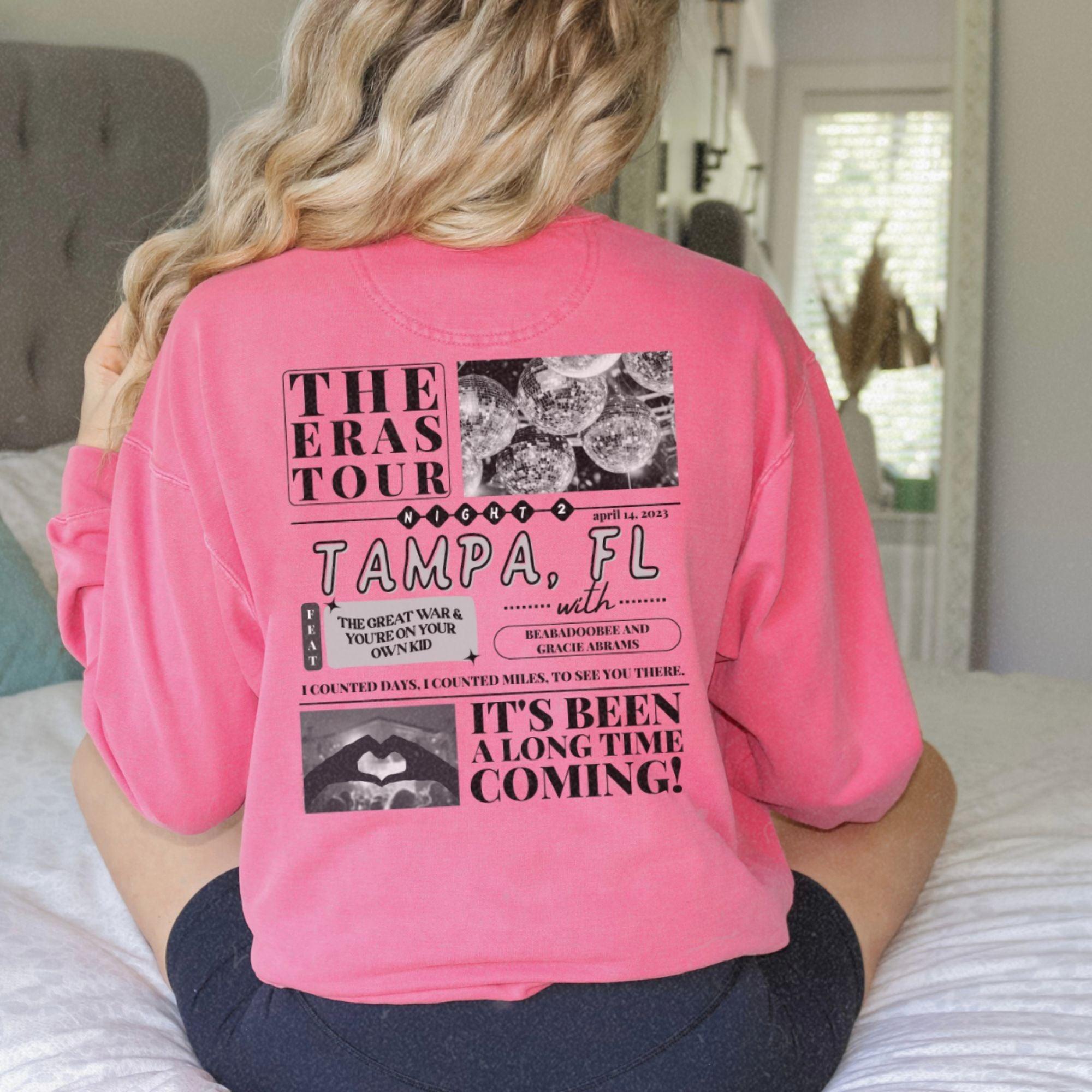 a woman sitting on a bed wearing a pink shirt