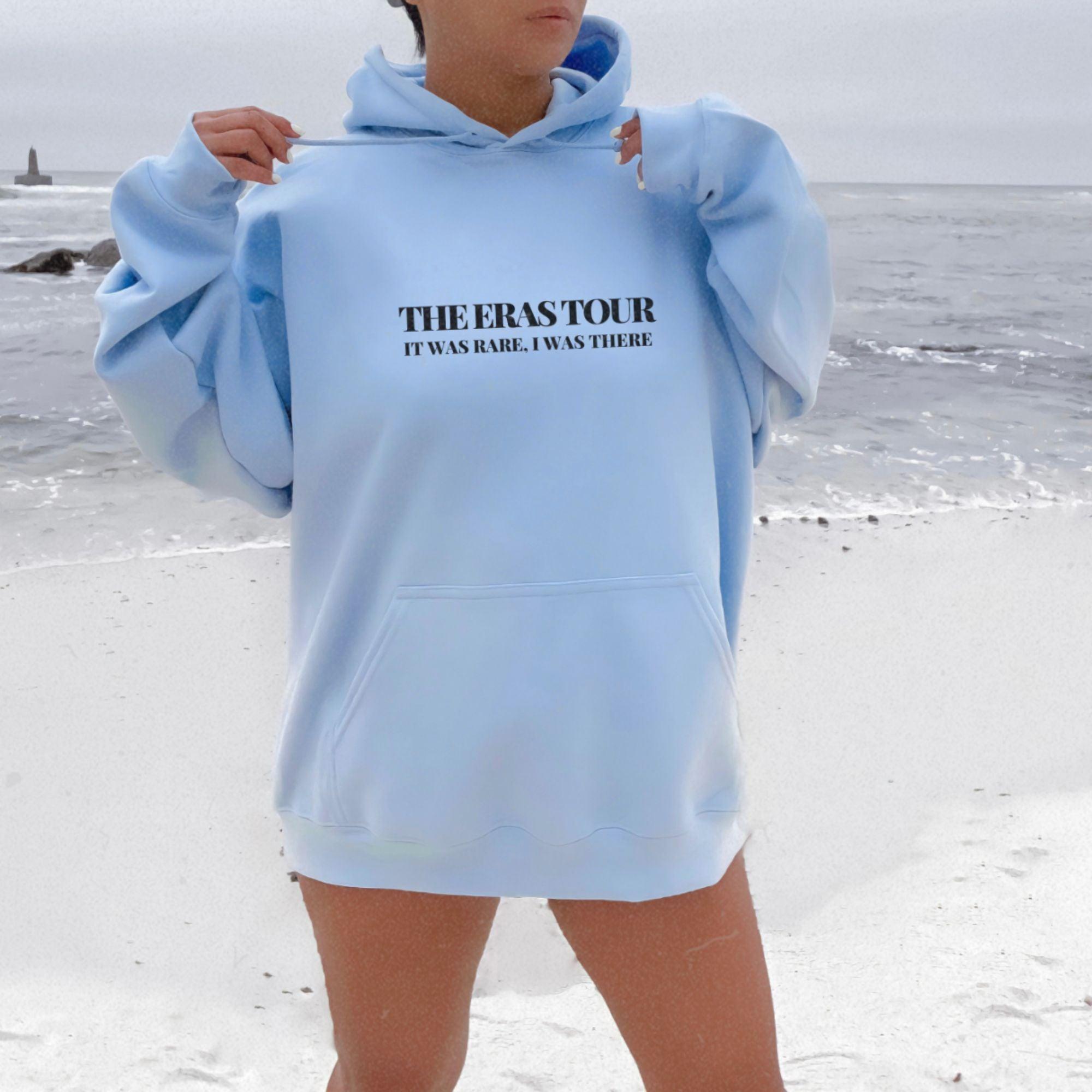 a woman standing on a beach wearing a blue sweatshirt