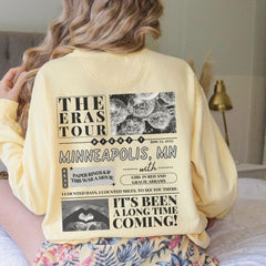 a woman sitting on a bed wearing a yellow sweatshirt