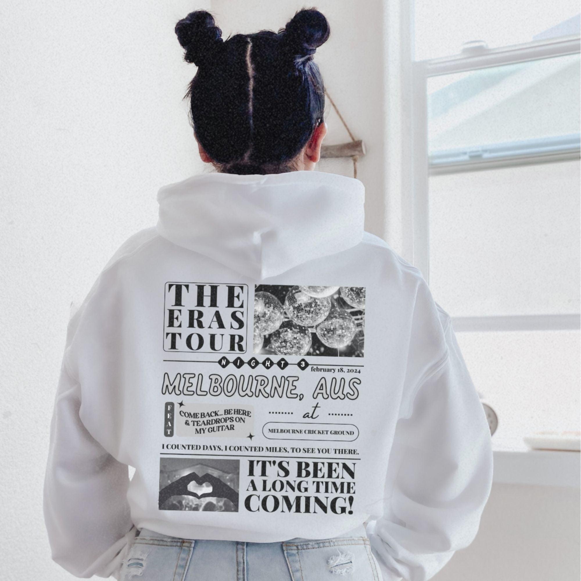 a woman wearing a white hoodie with the words the eras tour on it