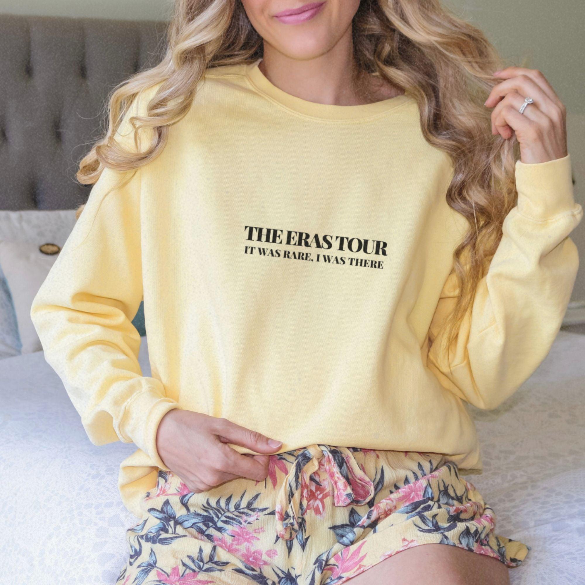a woman sitting on a bed wearing a yellow sweatshirt